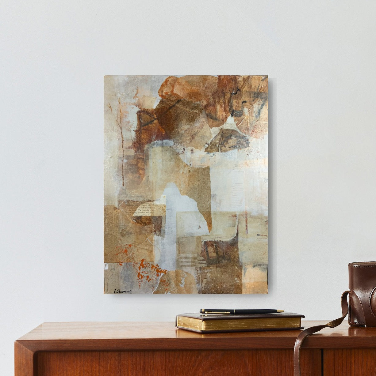 Deep Forest, an abstract mixed media painting, hangs in a modern office space. Its warm earth tones, organic textures, and blended elements complement the neutral decor, creating a sense of calm and sophistication. Subtle markings and aged paper details add depth, evoking the quiet mystery of nature within the workspace.