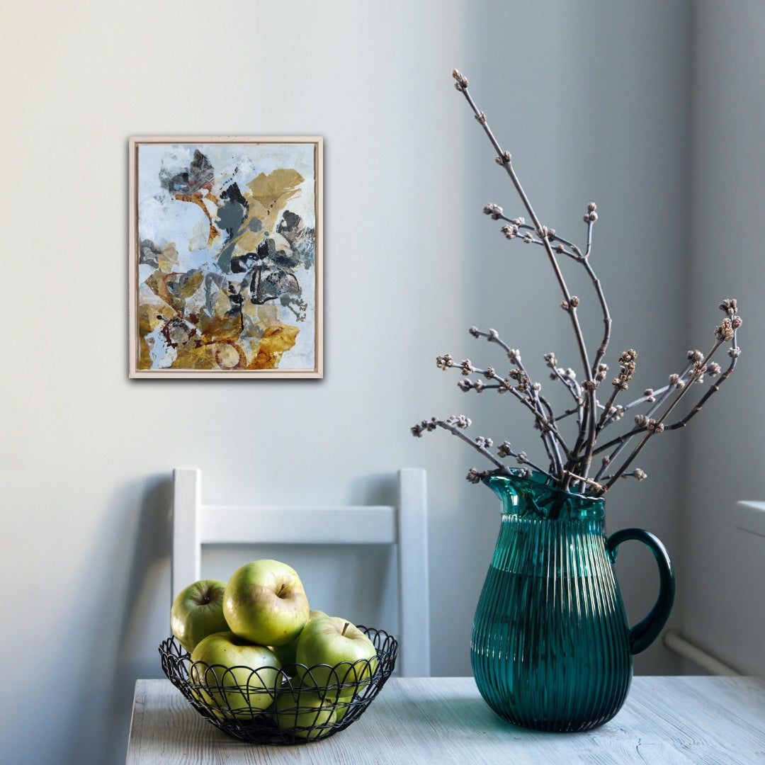 Teal pitcher with branches on a table next to apples and a chair, with a calming abstract nature painting in the background.