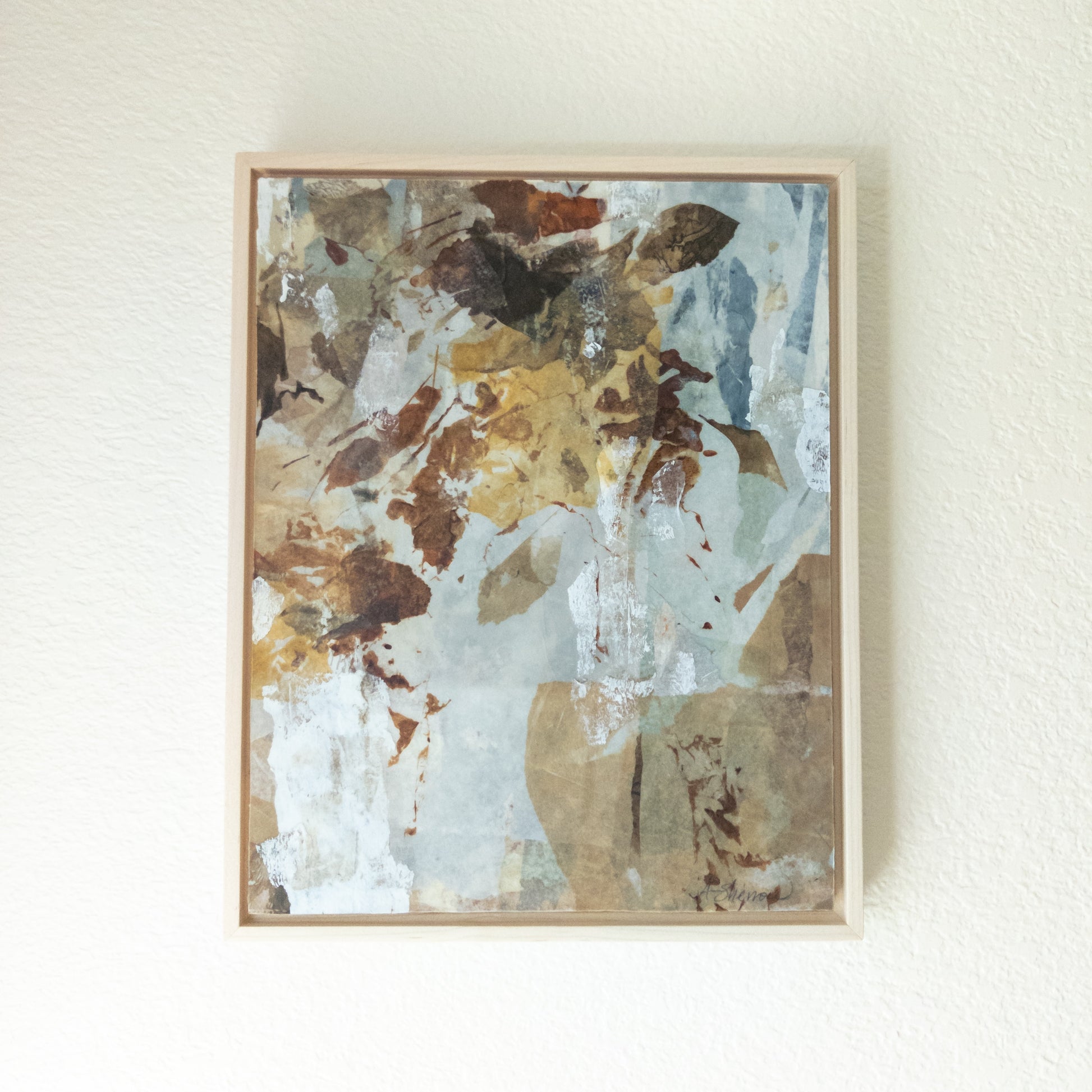Framed abstract art piece with earthy tones on a white wall