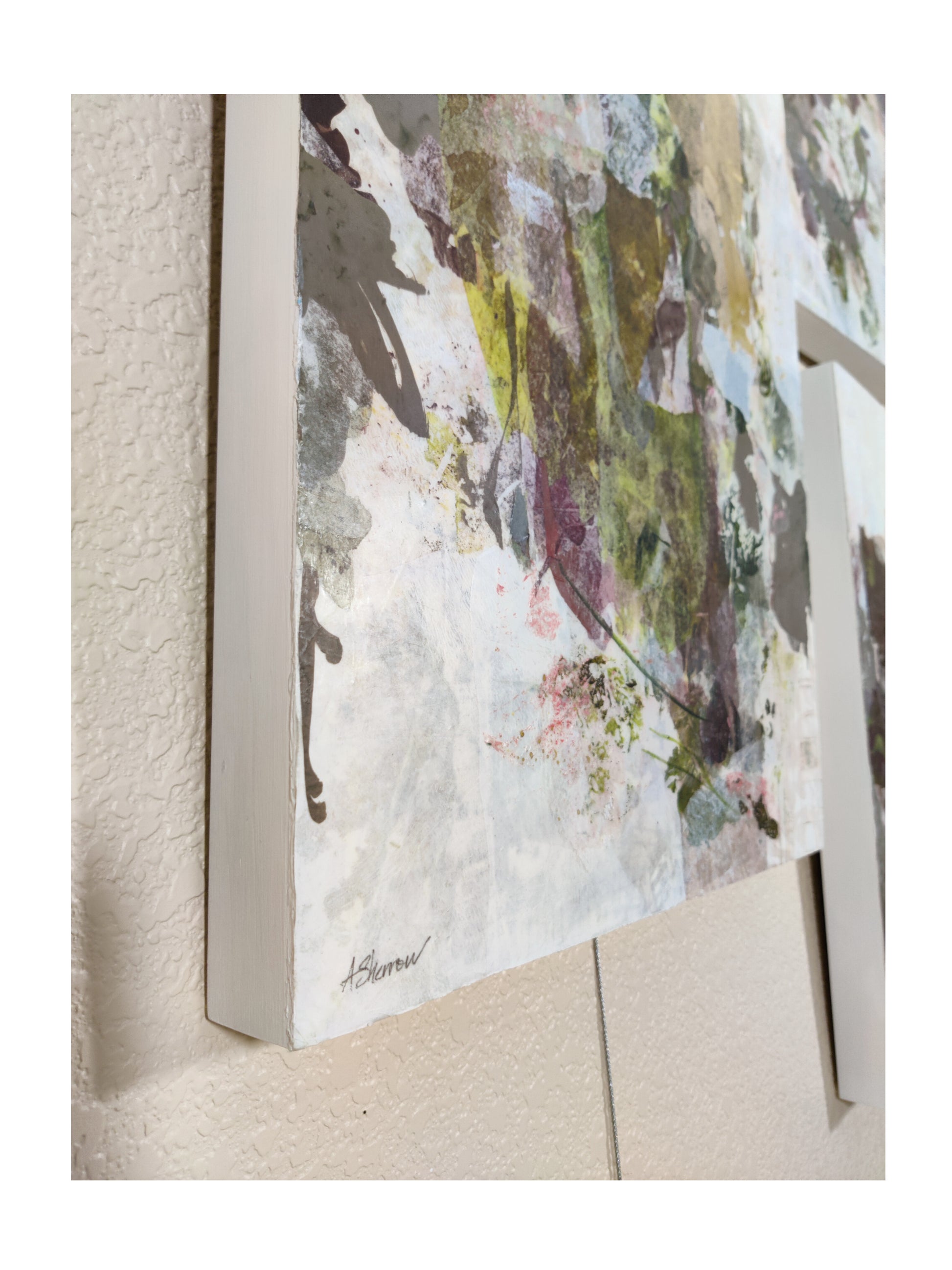 Abstract art piece with a white frame on a textured wall.